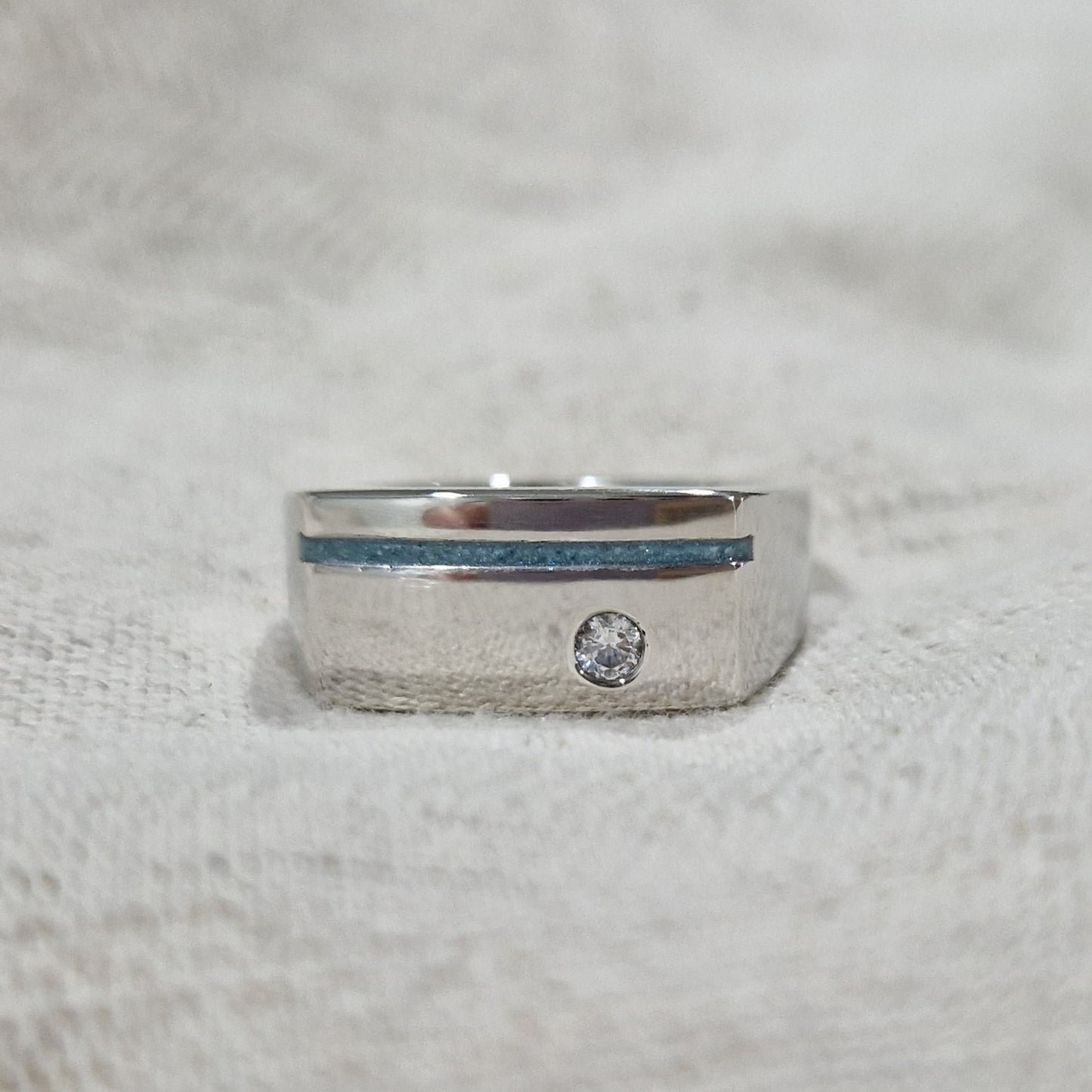 Ring als gedenksieraad met een streep aan de voorzijde, waar as of haar in verwerkt wordt. Ernaast is een zirkonia gezet. Alle