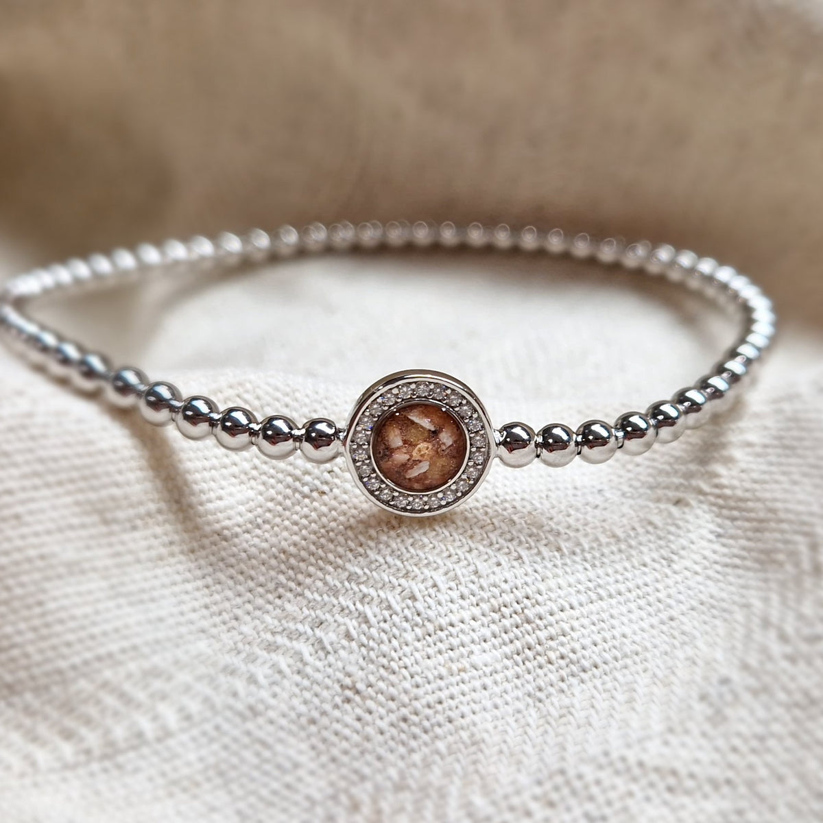 Flexibele as armband met rondje als compartiment gezet rondom met zirconia's voor as of haar. Alle