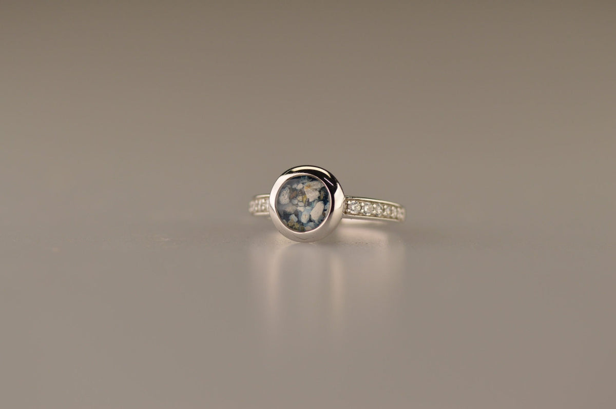 Gedenksieraad, ring 3 mm waar aan de bovenzijde zichtbaar as of haar verwerkt wordt. In de bovenste helft van de ringband zijn zirkonia's of diamanten naar keuze gezet. Alle
