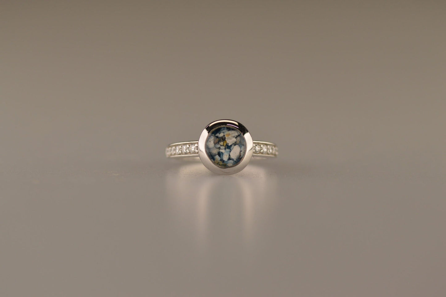 Gedenksieraad, ring 3 mm waar aan de bovenzijde zichtbaar as of haar verwerkt wordt. In de bovenste helft van de ringband zijn zirkonia's of diamanten naar keuze gezet. Alle