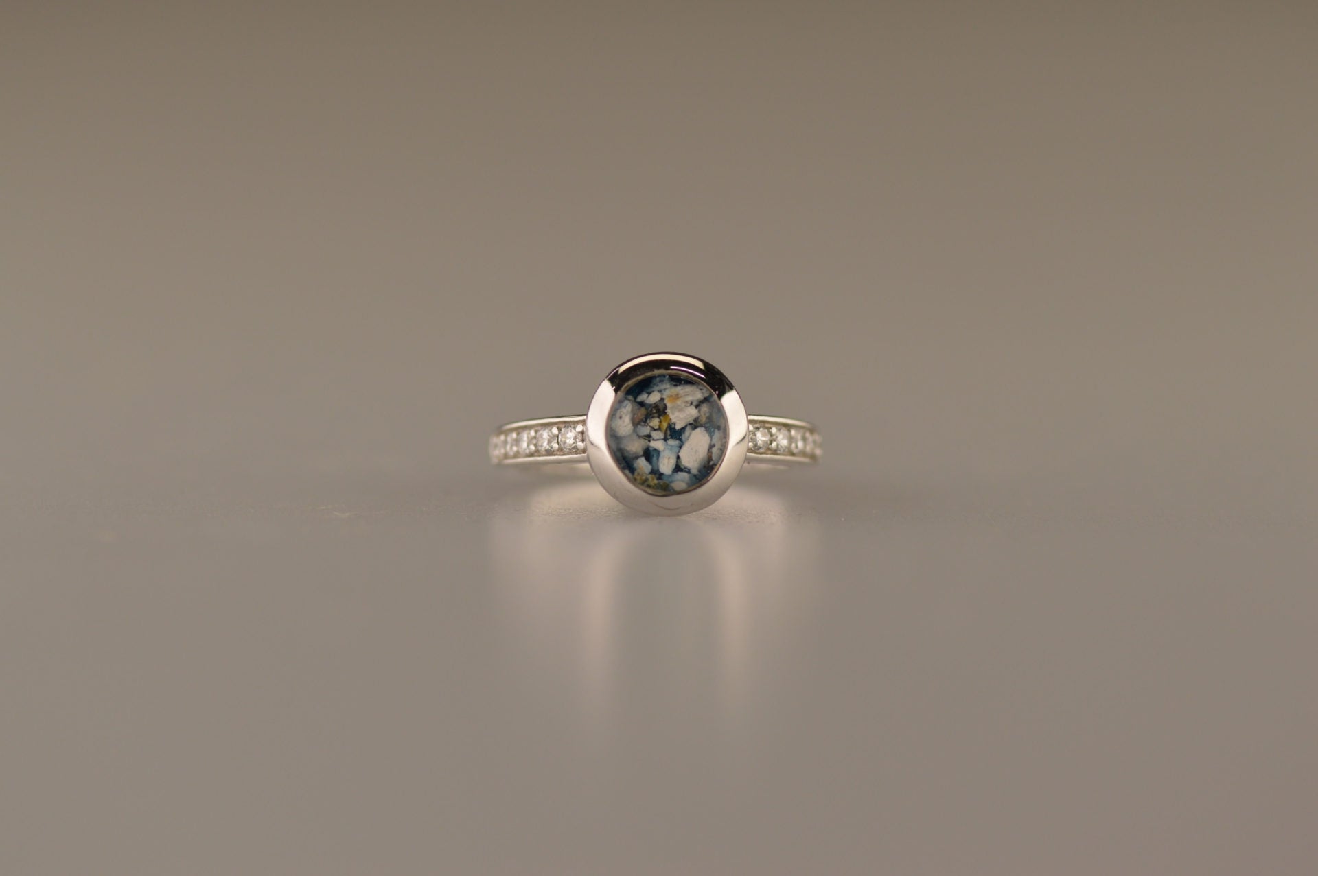 Gedenksieraad, ring 3 mm waar aan de bovenzijde zichtbaar as of haar verwerkt wordt. In de bovenste helft van de ringband zijn zirkonia's of diamanten naar keuze gezet. Alle