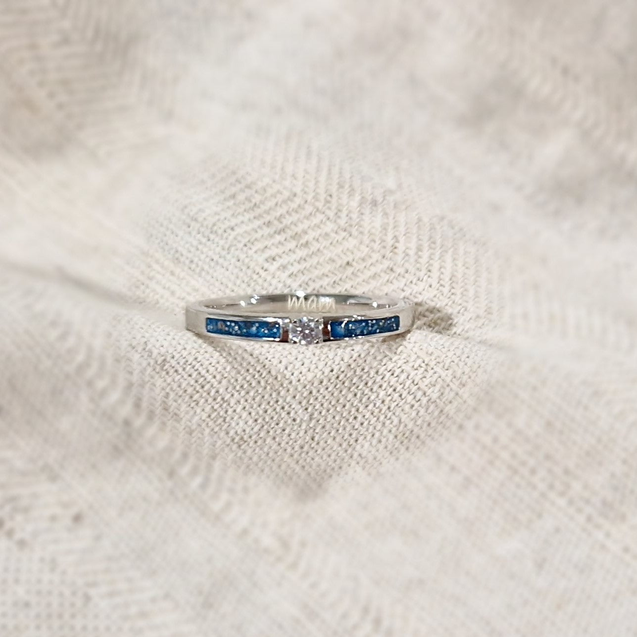 Gedenksieraad, ring 3 mm met (zirkonia of diamant), geflankeerd door twee compartimenten waar zichtbaar as of haar  in verwerkt wordt. Alle