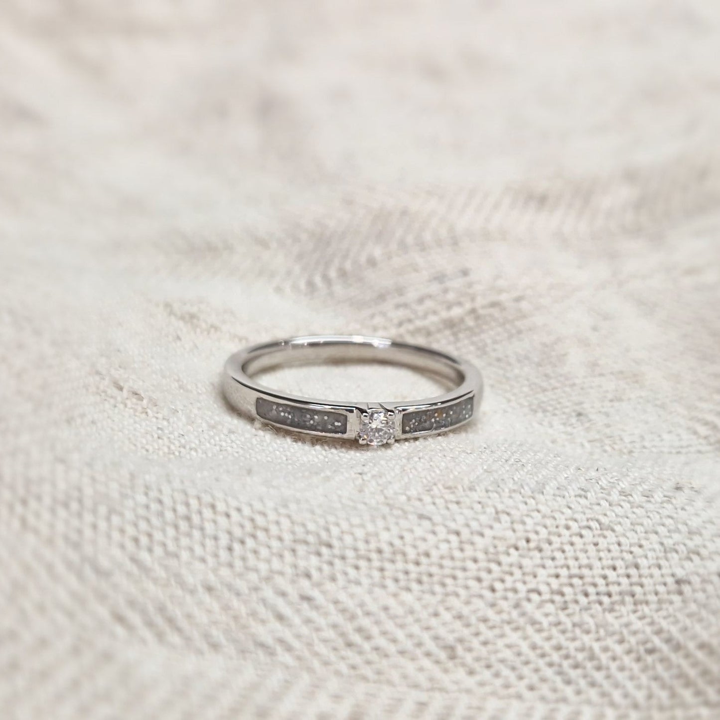 Gedenksieraad, ring 3 mm met (zirkonia of diamant), geflankeerd door twee compartimenten waar zichtbaar as of haar  in verwerkt wordt. Alle